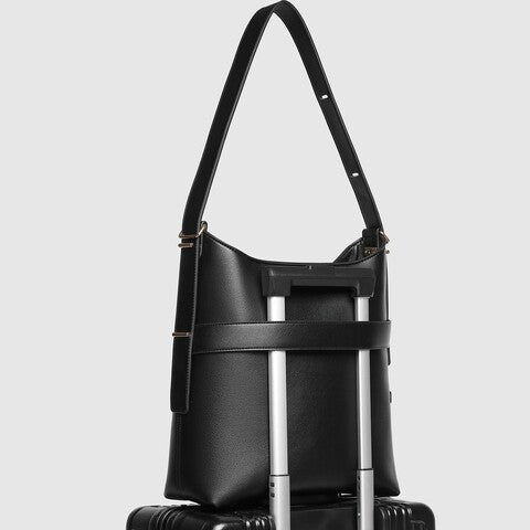 Black leather bag with a shoulder strap on top of a black suitcase 