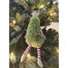 Fuzzy green Christmas tree ornament with striped legs hanging on a decorated tree.