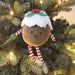 Christmas ornament shaped like a pudding with a face, hat, and striped socks hanging on a decorated tree.
