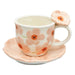 Ceramic cup with floral design on a matching saucer, featuring a decorative flower on the handle.